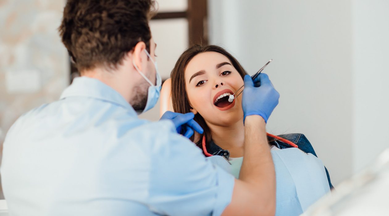 Dentist making professional teeth cleaning withb the cotton, female young patient at the dental office.